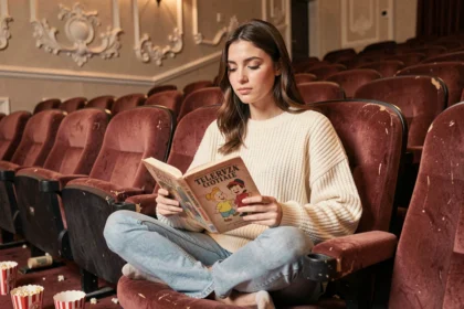 Jeune femme tenant un livre illustré de films Disney classiques dans une ancienne salle de cinéma aux fauteuils en velours rouge